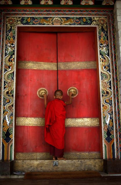 BHUTAN:THE LAST SHANGRI LA 2: A Buddhist monk enters the formidable doors of Trongsa Dzong, the Ancestral home of BhutanÕs monarchy. The Himalayan kingdom of Bhutan has sat in isolation for thousands of years and only recently has been thrust into the glare of modern times after centuries of solitude. Bhutan is a tiny, remote, and impoverished country wedged precariously between two powerful neighbors, India and China. Violent storms coming off the Himalaya gave the country its name, meaning "Land of the Thunder Dragon." This conservative Buddhist kingdom high in the Himalaya had no paved roads until the 1960s, was off-limits to foreigners until 1974, and launched television only in 1999 .